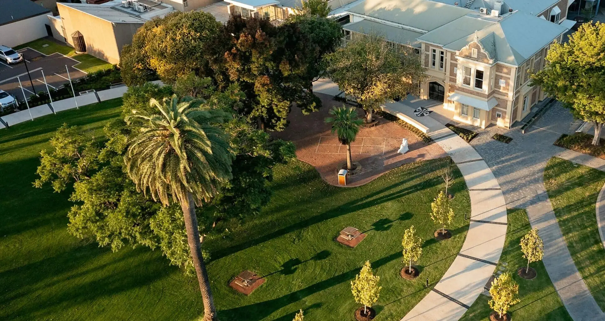 An aerial view of an independent school campus at golden hour: the heritage administration building, lawns, palms and the paths between them.